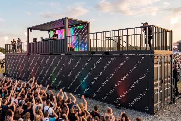 Mobile Bühne aus Seecontainern – Zweistöckig mit Branding-Fläche - Foto Zweistöckige mobile Bühne aus schwarzen Seecontainern mit DJ-Pult auf dem Oberdeck, LED-Screens, Geländer und großflächigem Branding auf einem Festival.