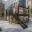 Foto Zweigeschossiger schwarzer Eventcontainer Pop-up Store Sustainable Living mit Holzverkleidung, Verglasung und Außentreppe auf einem gepflasterten Platz.