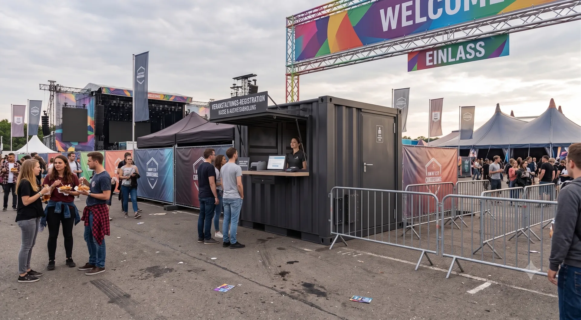 Bereit für den Ansturm: Unser Kassen- & Akkreditierungs-Container sorgt für einen organisierten Einlass und maximale Sicherheit auf Ihrem Event. Anthrazitfarbener Kassen- und Registrierungscontainer aus Übersee-Bauteilen auf einem Event-Einlassbereich mit geöffneter Verkaufsklappe, Counter-Arbeitsplatz für das Personal und vorgelagerten Absperrgittern unter einem Welcome-Schild.
